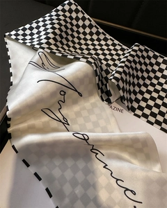 Detailed close-up of houndstooth silk scarf with elegant cursive print and smooth satin texture