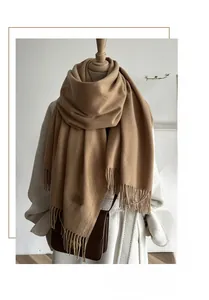 Detail of camel wool scarf with elegant tassels and leather tag on a beige coat