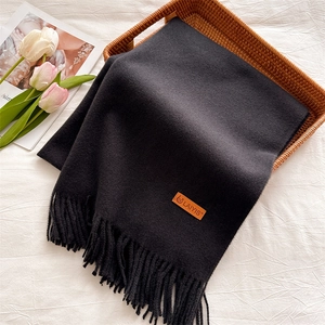 Detailed view of dark grey winter scarf with tassel fringe and leather tag in a basket