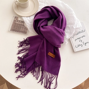 Detail of soft purple pashmina scarf with elegant fringe trim and brown leather brand tag