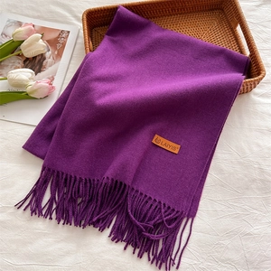 Close-up of deep purple winter scarf with fringe details and a leather logo label