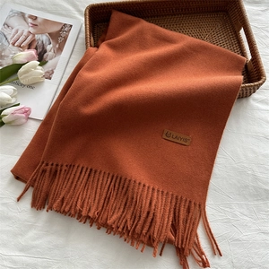 Detail of caramel orange wool scarf with fringe and leather logo on white texture