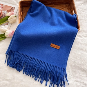Flat lay of royal blue fringed scarf with leather logo label in a woven basket
