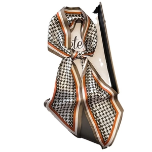 Classic houndstooth silk scarf with orange lettered border hanging on a white stand