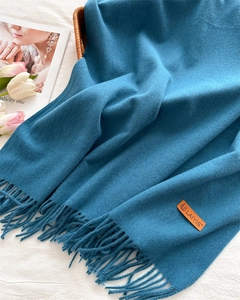 Detail of teal fringe scarf featuring a leather brand tag next to white tulips