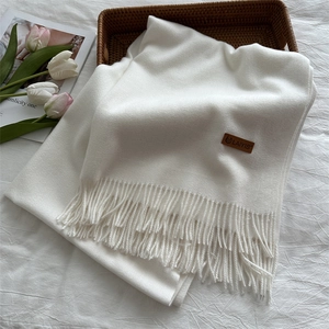 Detail of cream white scarf showing fringe edges and a brown leather brand tag