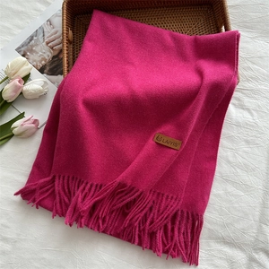 Close-up of thick rose red scarf with tassels and leather logo on aesthetic background