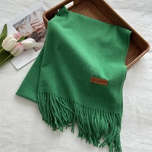 Close-up of bright green knitted scarf with fringes and brown leather brand label tag