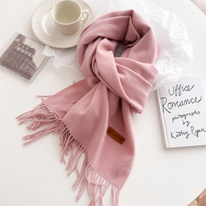 Detail view of light pink fringe scarf with leather brand label and cozy winter accessories