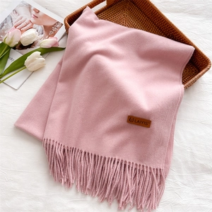 Close-up of pink cashmere-soft scarf with fringe edges and premium leather logo tag