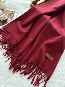 Detail of dark red knit scarf with soft texture, fringes and a small leather brand tag