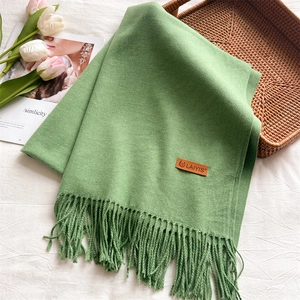 Detail of light green knit scarf with fringe edges and premium leather brand logo tag