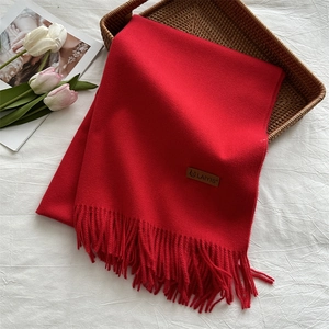 Detailed view of red knitted scarf with fringe and brand tag on a woven tray