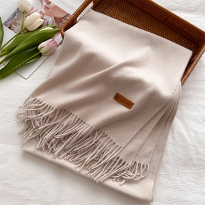 Detail of beige tassel scarf with leather logo patch in a rustic wicker basket