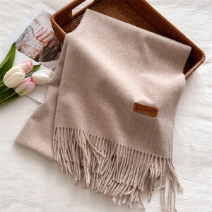 Close-up of soft beige tassel scarf with premium leather brand tag on a rustic tray