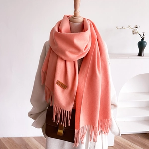 Coral orange winter scarf with fringe details and leather label on beige coat