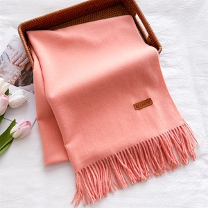Detail of soft pink knitted scarf with tassels and leather label on white fabric
