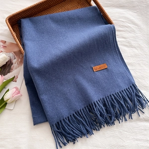 Close-up of deep blue scarf with fringes and leather label in a woven basket
