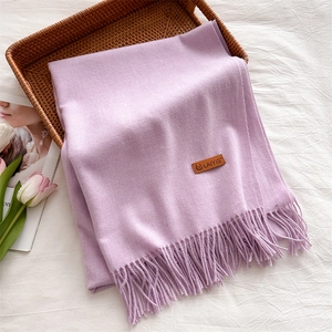 Close-up of light purple scarf with long fringes and leather logo tag on a rattan tray