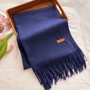 Detail of dark blue cashmere scarf with brown leather logo tag and fringed edges
