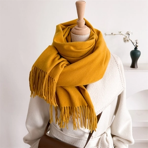 Detail of ginger yellow knitted scarf with long fringe tassels on a wooden mannequin