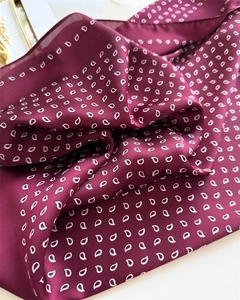 Macro detail of wine red silk scarf featuring classic white paisley drop patterns