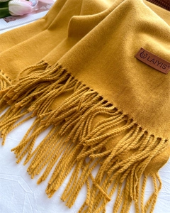 Close-up of ginger yellow knit scarf with fringe detail and brown leather logo tag