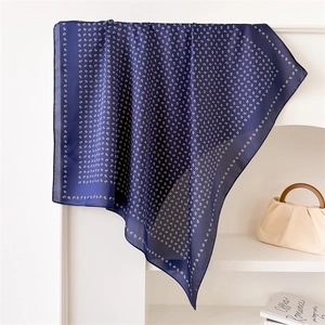Detailed view of dark blue paisley silk scarf draped over a white surface with props