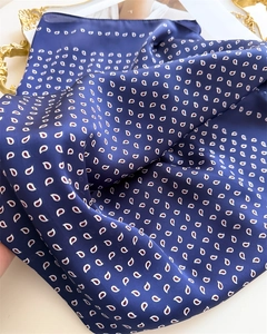 Detail of navy blue silk-like square scarf with elegant paisley patterns on a gold tray