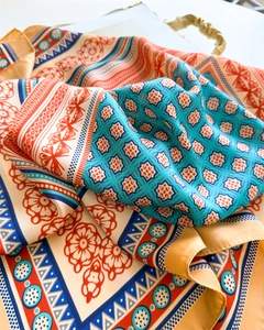 Detail shot of the silky printed square scarf with colorful geometric patterns on a tray