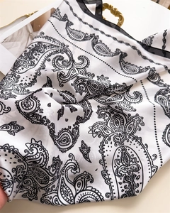 Nahaufnahme des weißen Seidenschals mit schwarzen Paisley-Mustern und feiner Umrandung