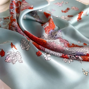 Detail of light blue silk scarf with vibrant floral patterns and smooth satin texture