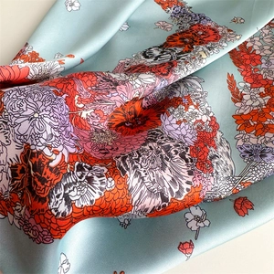 Detailed close-up of light blue silk scarf with vibrant orange poppy floral pattern