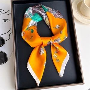 Macro shot of vibrant orange silk scarf featuring delicate floral peony patterns on tray
