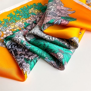 Macro shot of orange floral silk scarf showing satin texture and hand-painted pattern