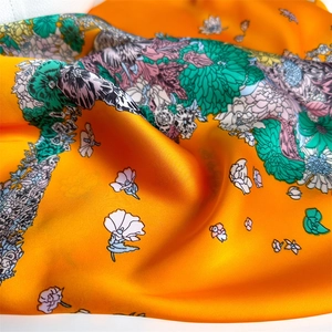 Detail of vibrant orange floral silk scarf showing elegant satin texture and intricate prints