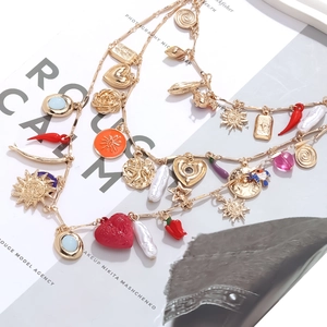Detail of layered gold necklaces with red heart pearl and chili charms on a magazine