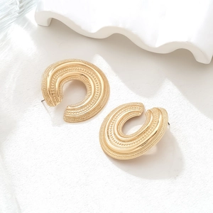 Detail of vintage gold C-shape earrings with intricate beaded texture on stone surface