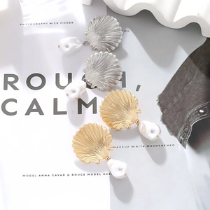 Macro detail of gold and silver seashell baroque pearl earrings on a magazine background