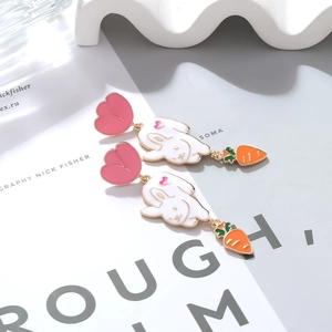 Close-up of cute enamel bunny and carrot drop earrings on a stylish lifestyle background