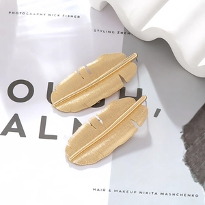 Close-up of golden banana leaf earrings showing detailed brushed metal texture