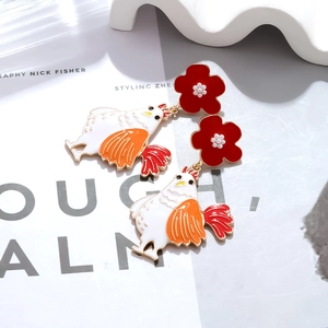 Detalle de pendientes asimétricos esmaltados con motivos de gallina y flores rojas