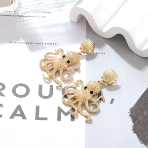 Macro detail of gold octopus earrings with shell stud and matte enamel texture