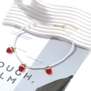 Detail of beaded necklace featuring red strawberry charms and white faux pearls