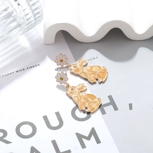 Detail of daisy stud earrings with golden rabbit pendants on a stylish magazine layout