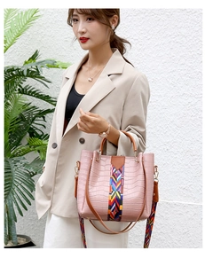 Detail of pink croc-embossed bucket bag with colorful woven strap and gold hardware