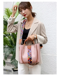 Pink croc bucket bag with wide embroidered strap and brown handles on casual model