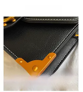 Detail der schwarzen Ledertasche mit goldenen Metallecken und weißer Kontrastnaht im Fokus