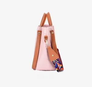 Close-up of pink faux crocodile leather bucket bag with wide colorful geometric strap