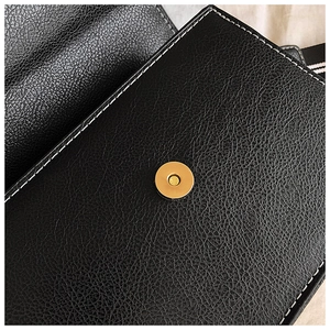 Detail von schwarzem Leder mit Litschi-Maserung, weißen Nähten und goldener Magnetschließe